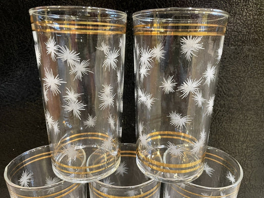 Set de pichel con 4 vasos de vidrio transparente con diseño floral grabado y borde dorado.