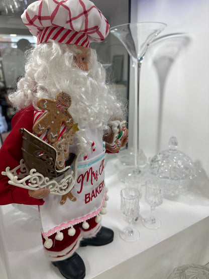 Santa Claus 
Figura de  48 cm, edición 2023 de North Pole Trading. Forma parte de la colección Fabriché y representa a Santa como chef de galletas, con gorro a cuadros rojos y blancos y delantal blanco.