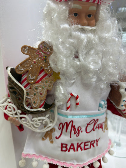 Santa Claus 
Figura de  48 cm, edición 2023 de North Pole Trading. Forma parte de la colección Fabriché y representa a Santa como chef de galletas, con gorro a cuadros rojos y blancos y delantal blanco.