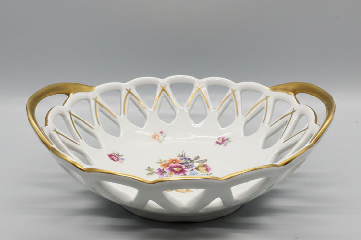 Esta pieza es un cuenco calado (Panera) de porcelana vintage con motivos florales y bordes dorados.