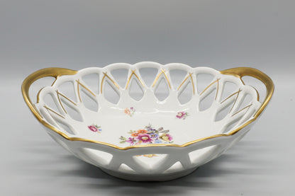 Esta pieza es un cuenco calado (Panera) de porcelana vintage con motivos florales y bordes dorados.