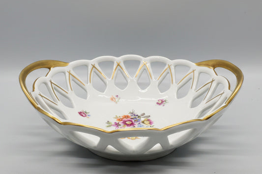 Esta pieza es un cuenco calado (Panera) de porcelana vintage con motivos florales y bordes dorados.