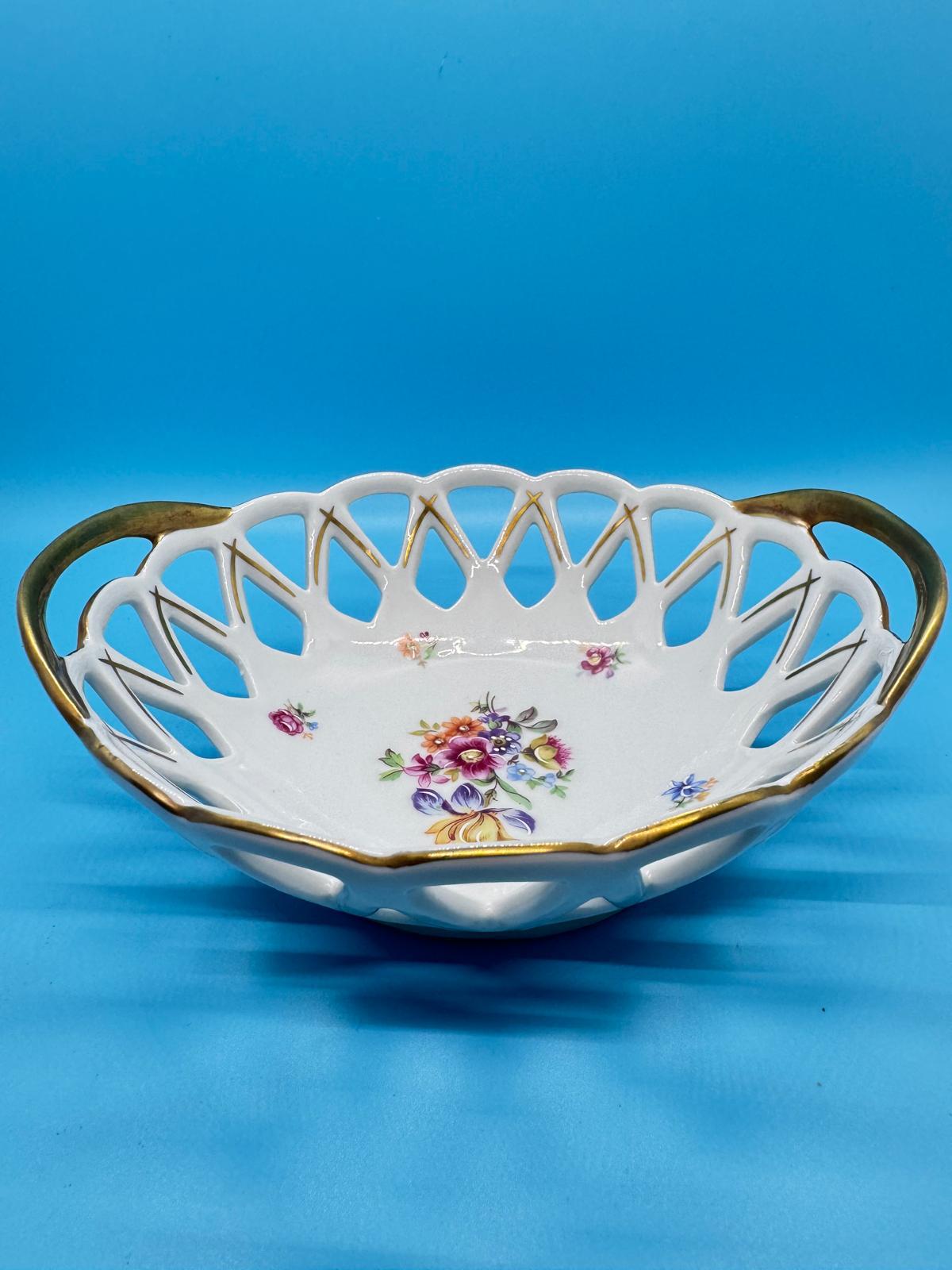 Esta pieza es un cuenco calado (Panera) de porcelana vintage con motivos florales y bordes dorados.