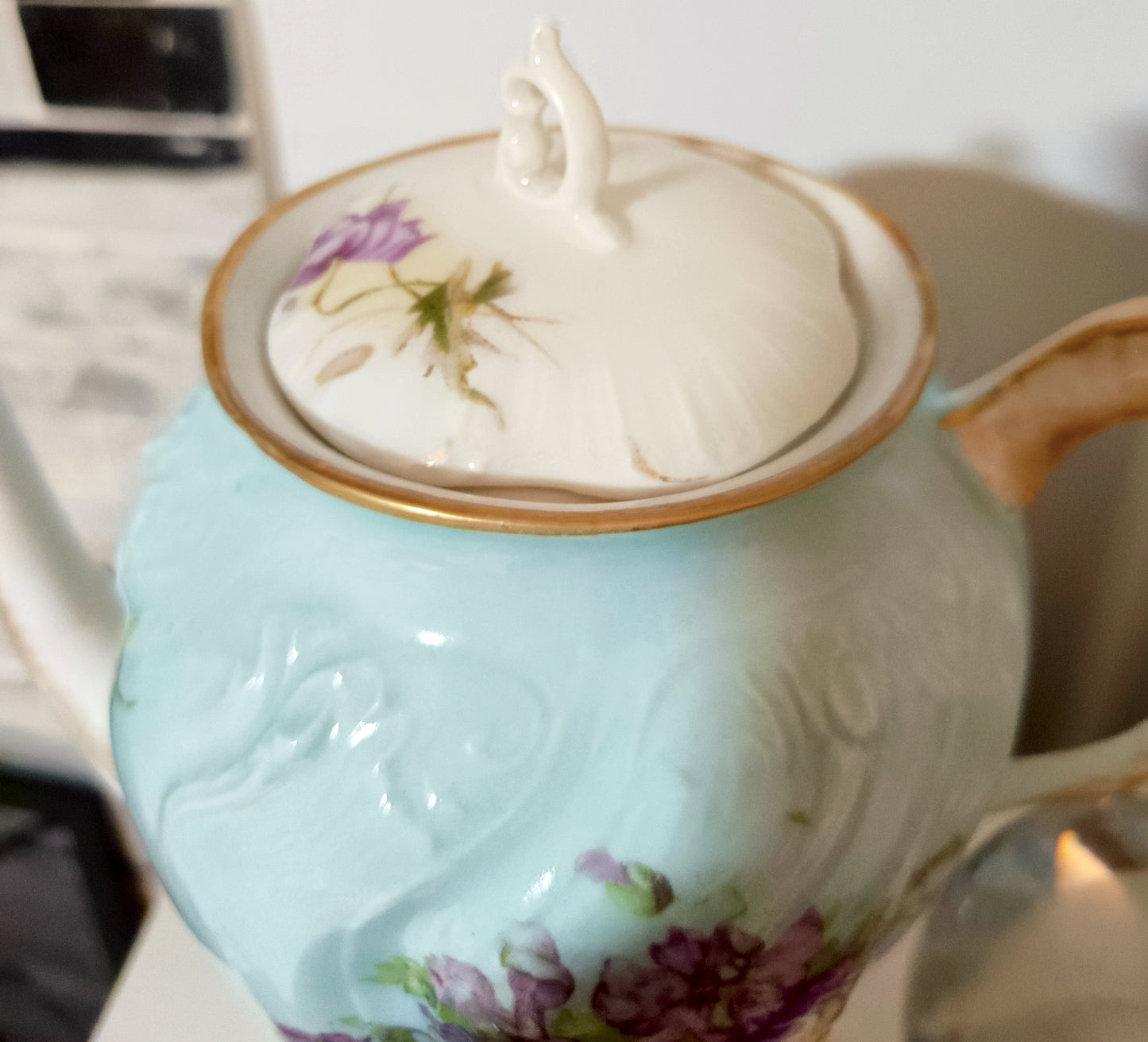 La tetera de Chamart Limoges France mide 18cm de alto y está elaborada en porcelana pintada a mano, destacando un elegante motivo floral en tonos rosa y lavanda, con detalles dorados sobre un fondo verde menta pálido.