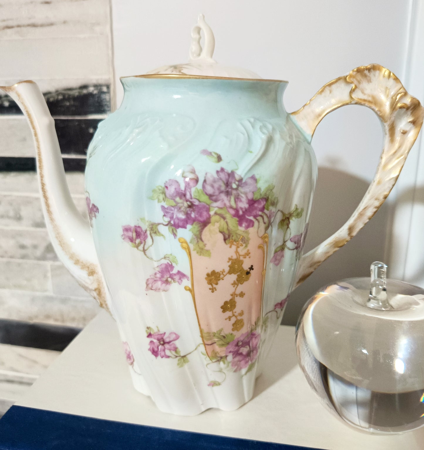 La tetera de Chamart Limoges France mide 18cm de alto y está elaborada en porcelana pintada a mano, destacando un elegante motivo floral en tonos rosa y lavanda, con detalles dorados sobre un fondo verde menta pálido.