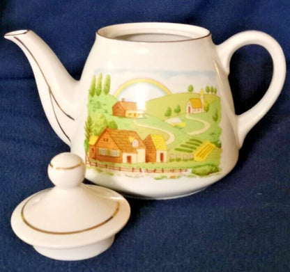 La tetera de cerámica vintage, fabricada en Japón, presenta un diseño de paisaje rural pintado a mano y un borde plateado. 11cm de alto 10cm diámetro.