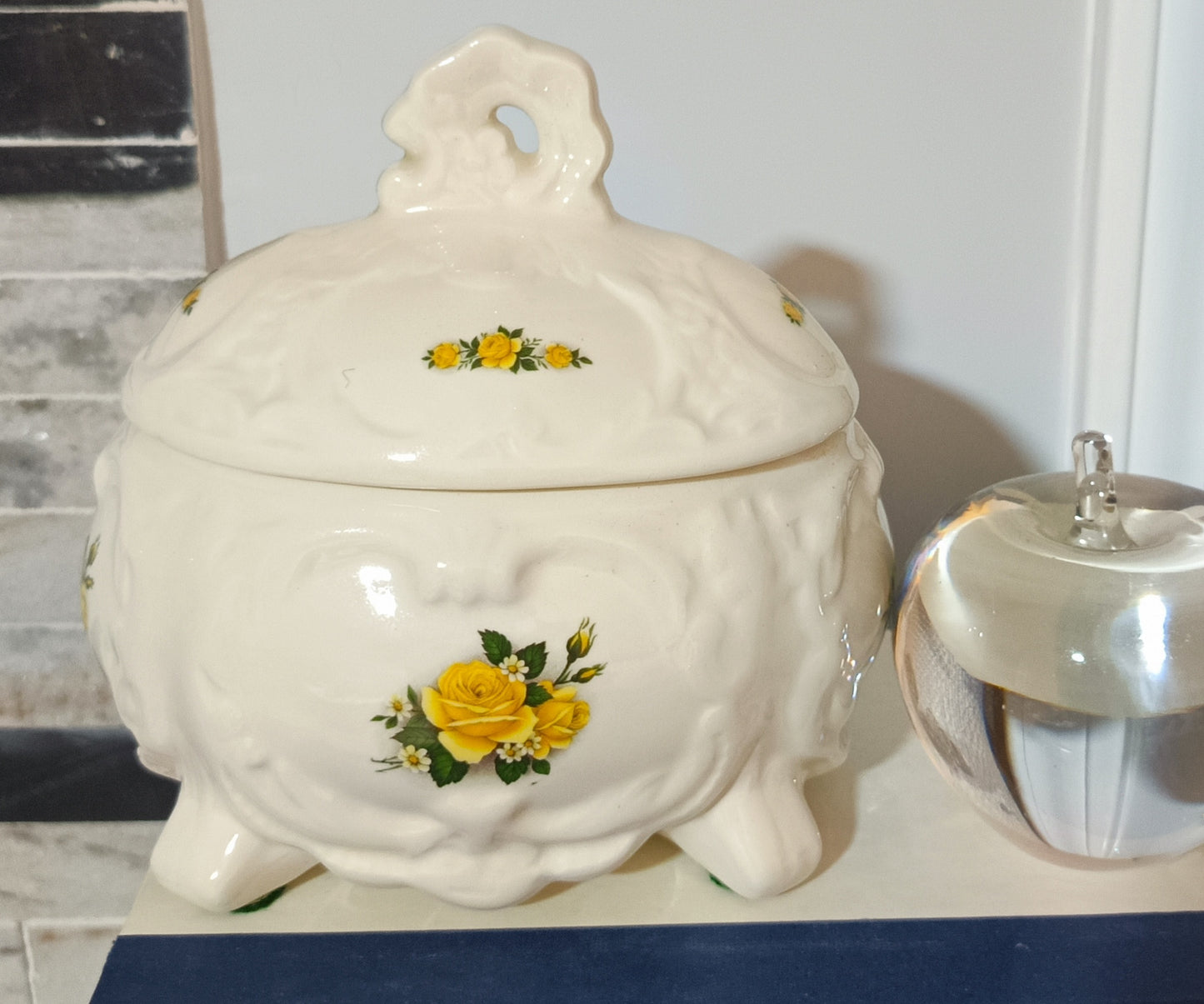 Joyero o bombonera de cerámica blanca presenta un diseño victoriano con relieve ondulado con rosas amarillas pintadas a mano. Medidas 17cm alto 10cm ancho de 13cm largo.