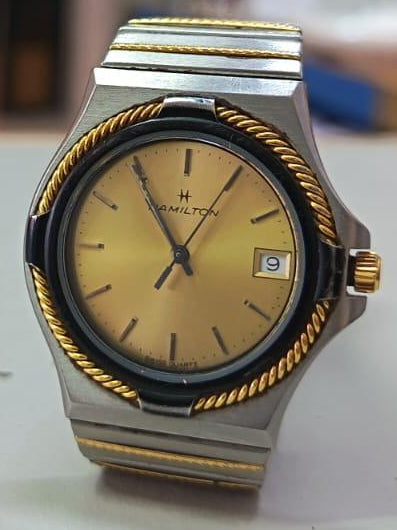 Reloj de cuarzo Hamilton de acero inoxidable de tres tonos (plateado y dorado) con un bisel de cuerda trenzada y esfera dorada.