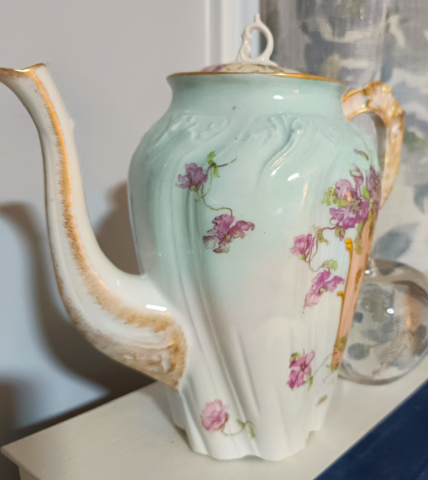 La tetera de Chamart Limoges France mide 18cm de alto y está elaborada en porcelana pintada a mano, destacando un elegante motivo floral en tonos rosa y lavanda, con detalles dorados sobre un fondo verde menta pálido.