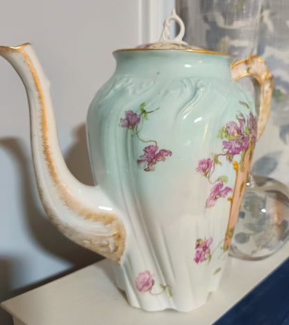 La tetera de Chamart Limoges France mide 18cm de alto y está elaborada en porcelana pintada a mano, destacando un elegante motivo floral en tonos rosa y lavanda, con detalles dorados sobre un fondo verde menta pálido.
