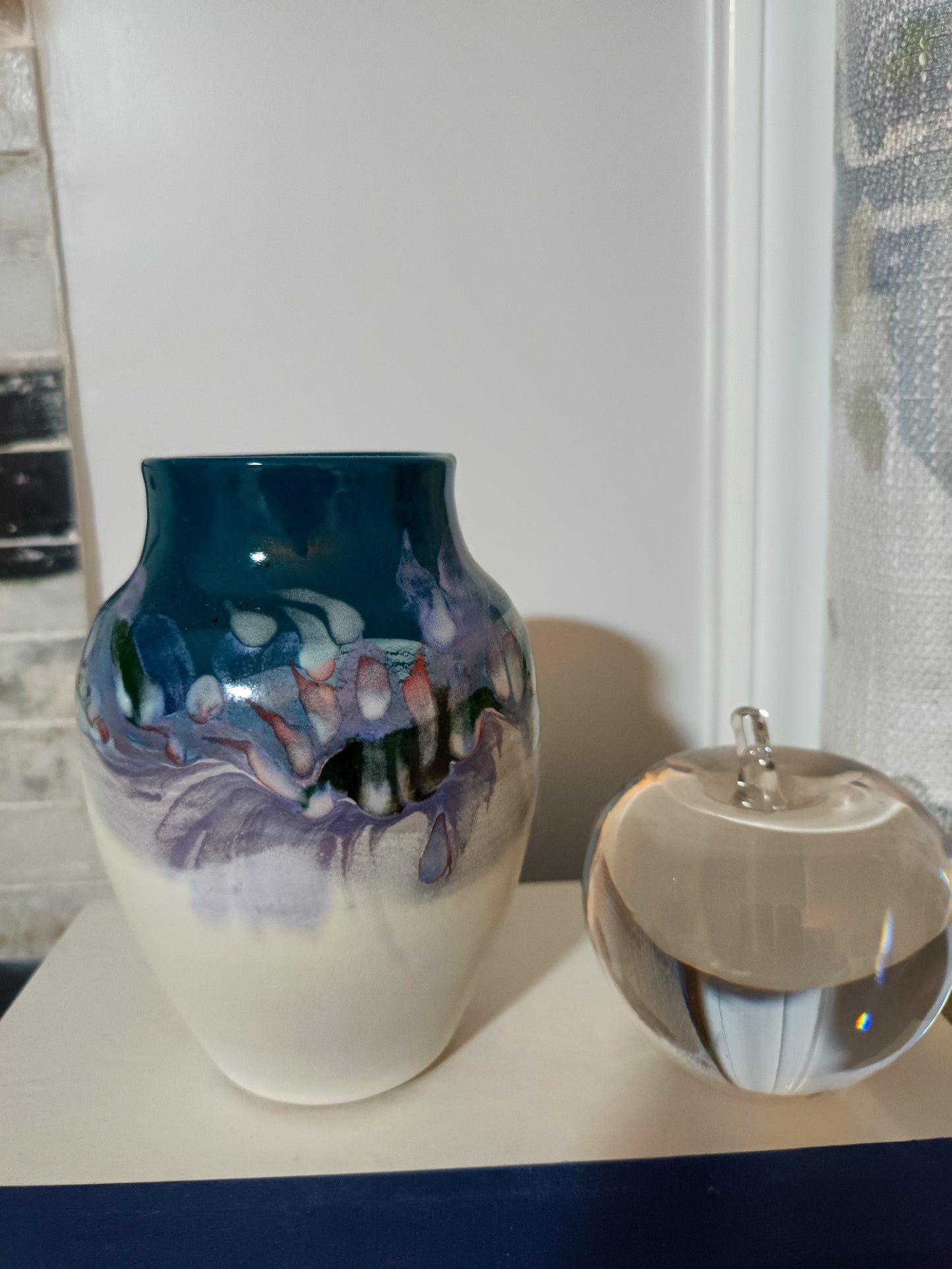 Este jarrón- florero de cerámica artística mide 16 cm de alto y presenta un diseño contemporáneo con un esmaltado en tonos azulados, verdosos y violetas, complementado por una base mate de arcilla clara.