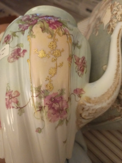 La tetera de Chamart Limoges France mide 18cm de alto y está elaborada en porcelana pintada a mano, destacando un elegante motivo floral en tonos rosa y lavanda, con detalles dorados sobre un fondo verde menta pálido.