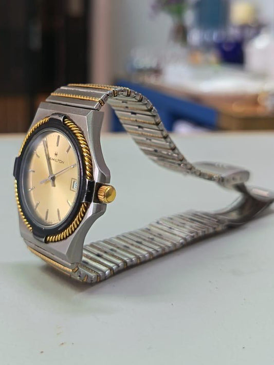 Reloj de cuarzo Hamilton de acero inoxidable de tres tonos (plateado y dorado) con un bisel de cuerda trenzada y esfera dorada.