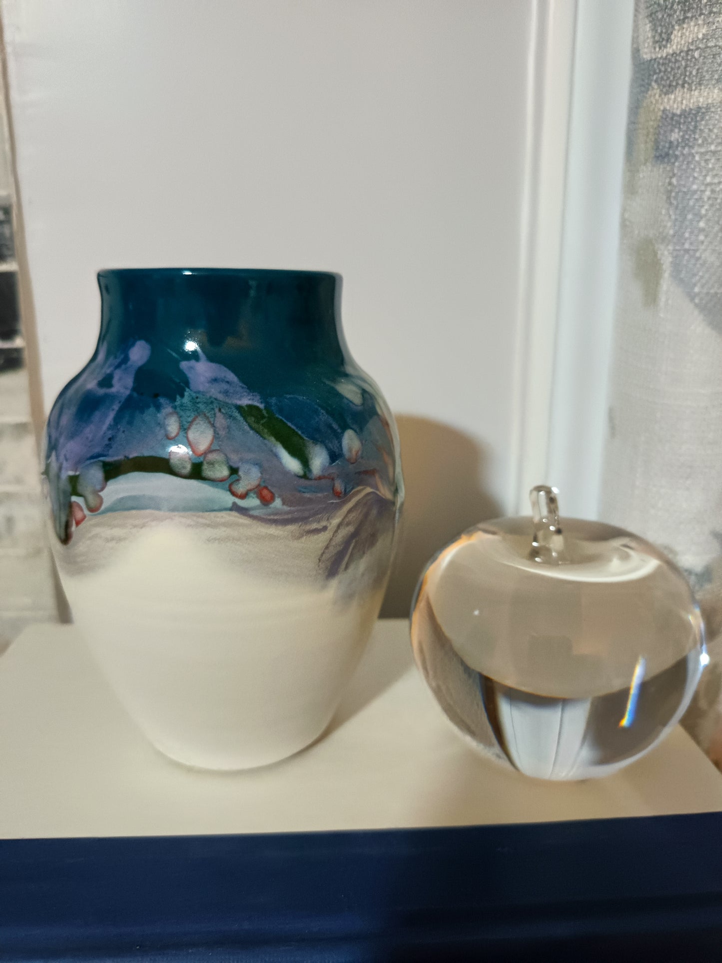 Este jarrón- florero de cerámica artística mide 16 cm de alto y presenta un diseño contemporáneo con un esmaltado en tonos azulados, verdosos y violetas, complementado por una base mate de arcilla clara.