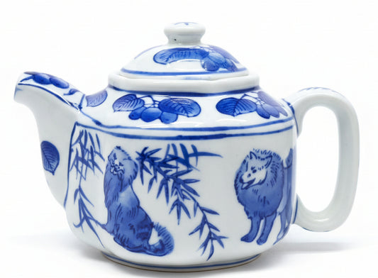 Tetera vintage de porcelana azul y blanca presenta un diseño elegante de perros y árboles frutales, complementada por una forma de flor.