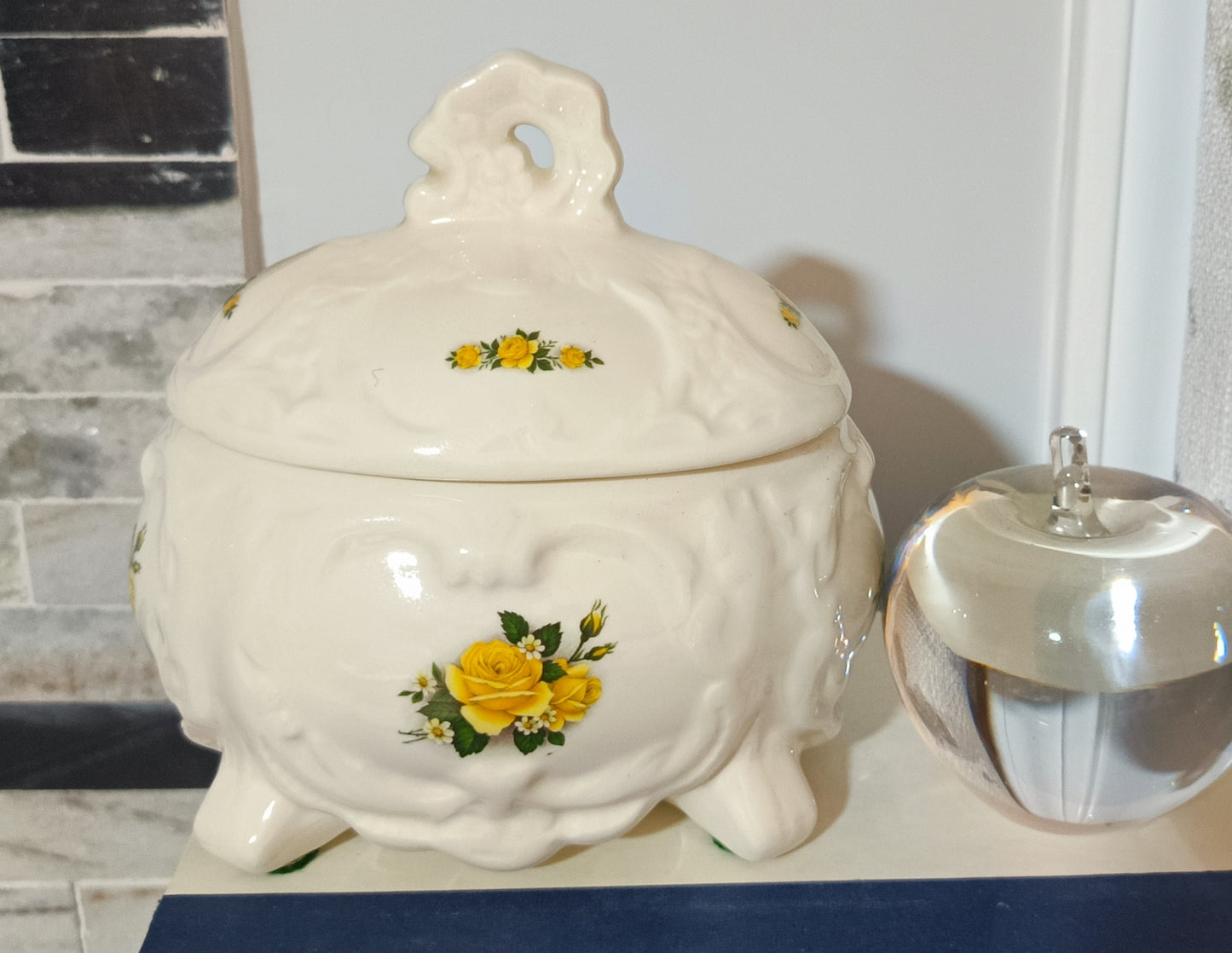 Joyero o bombonera de cerámica blanca presenta un diseño victoriano con relieve ondulado con rosas amarillas pintadas a mano. Medidas 17cm alto 10cm ancho de 13cm largo.
